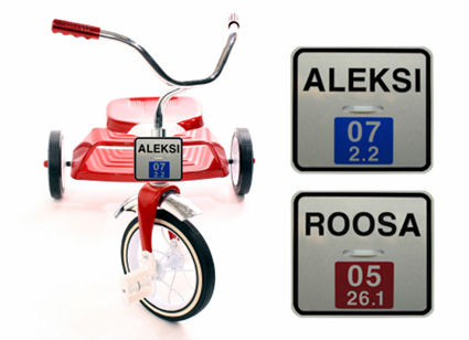 Punainen kolmipyörä, jonka ohjaustankoon on kiinnitetty ALEKSI-rekkari, sekä lähikuvat ALEKSI- ja ROOSA-kilvistä